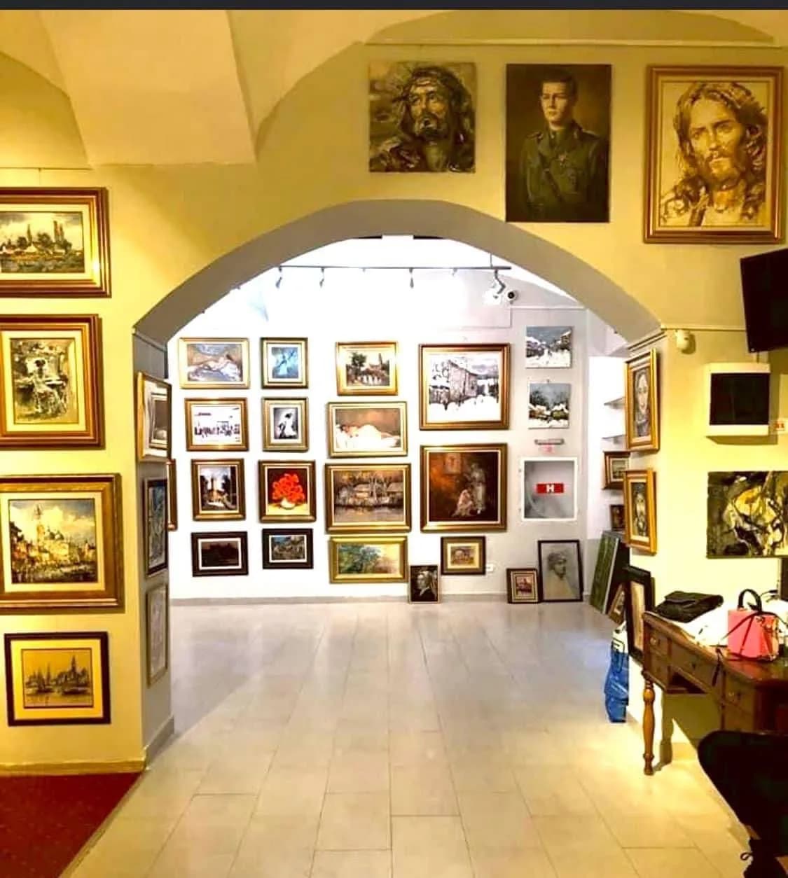 Sala Galeriei MoMart, cu pereții plini de tablouri în rame aurii, sub o arcadă boltită