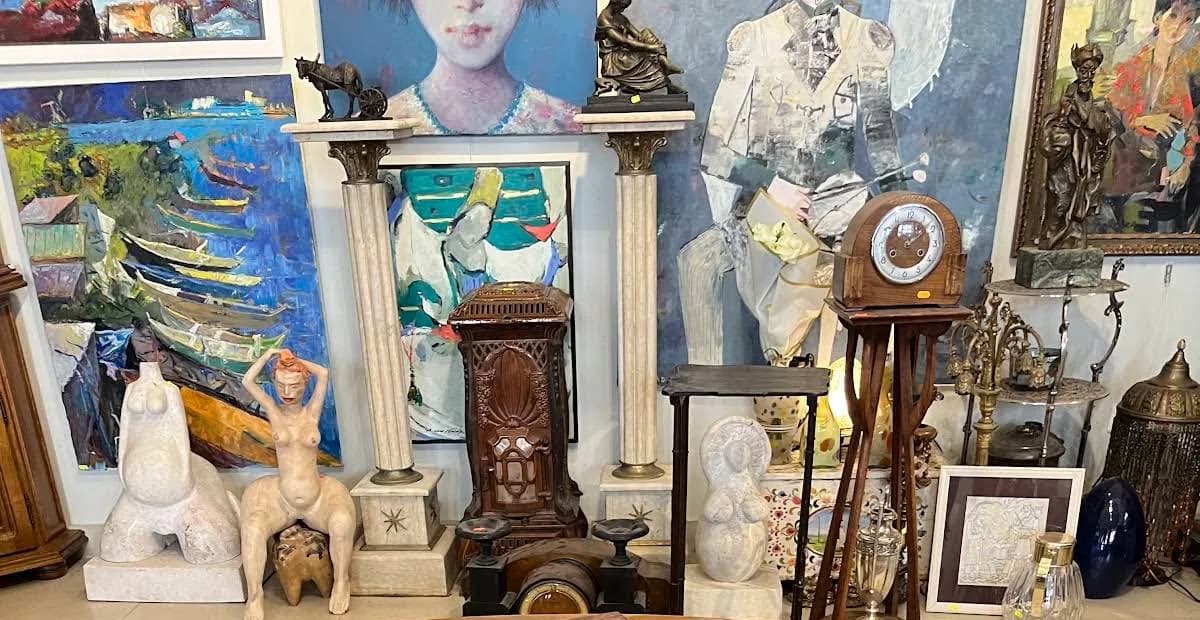 Perete de galerie plin de tablouri de mărimi diferite, cu sculpturi de piatră pe socluri de marmură în fața lui