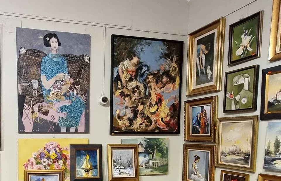 Perete de galerie plin de tablouri: două pânze mari nerămate în stânga și un grup des de lucrări mici în rame aurii și negre în dreapta