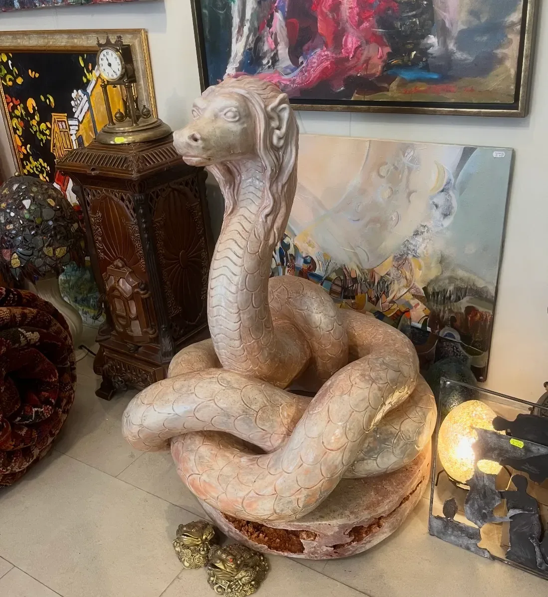 Sculptură de ceramică înaltă cât un om: un șarpe încolăcit, cu cap de animal cu coamă și solzi mari, așezat pe podeaua galeriei