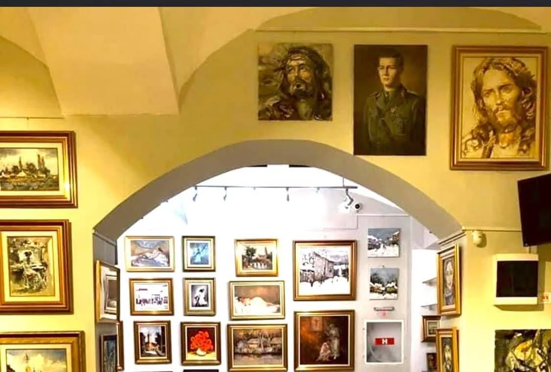 Arcadă albă într-o sală boltită, cu pereții acoperiți de tablouri în rame aurii și o a doua sală luminată dincolo de arc